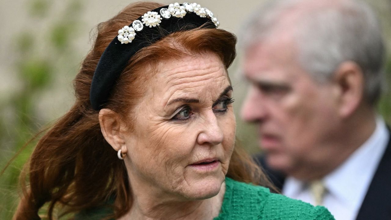 Sarah Ferguson wearing a green coat and black crystal headband looking to the right while Prince Andrew is blurry behind her