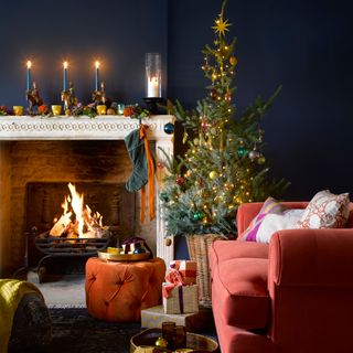 Rich toned living room with a decorated Christmas tree and blue candles on the fireplace