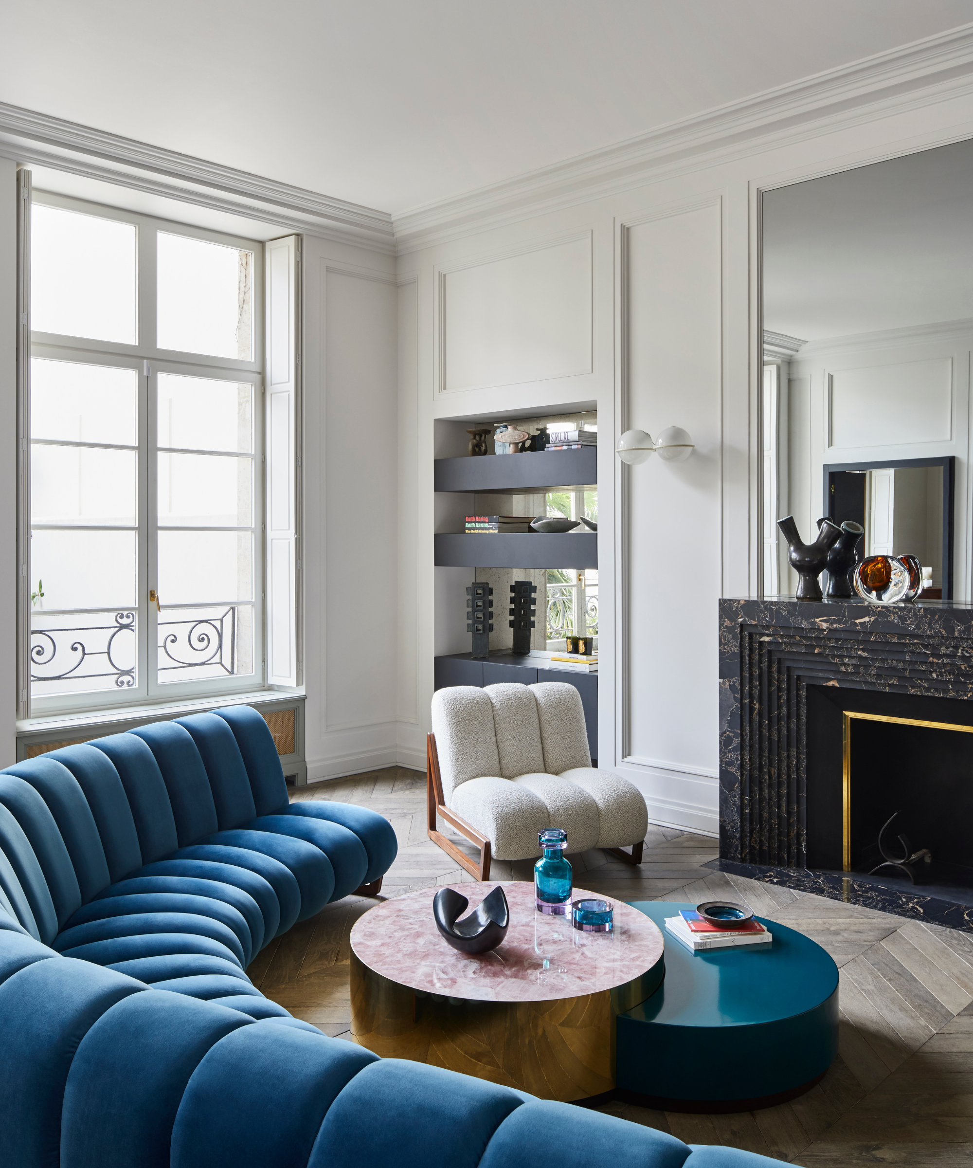 Curved petrol blue tufted couch in modern living room with white armchair in front of statement fireplace