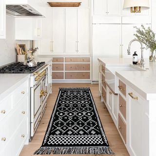 A black rug with a white diamond pattern sits on wooden floor in a white kitchen