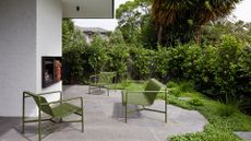 A garden with a seating area and outdoor in-wall fireplace with green metal chairs