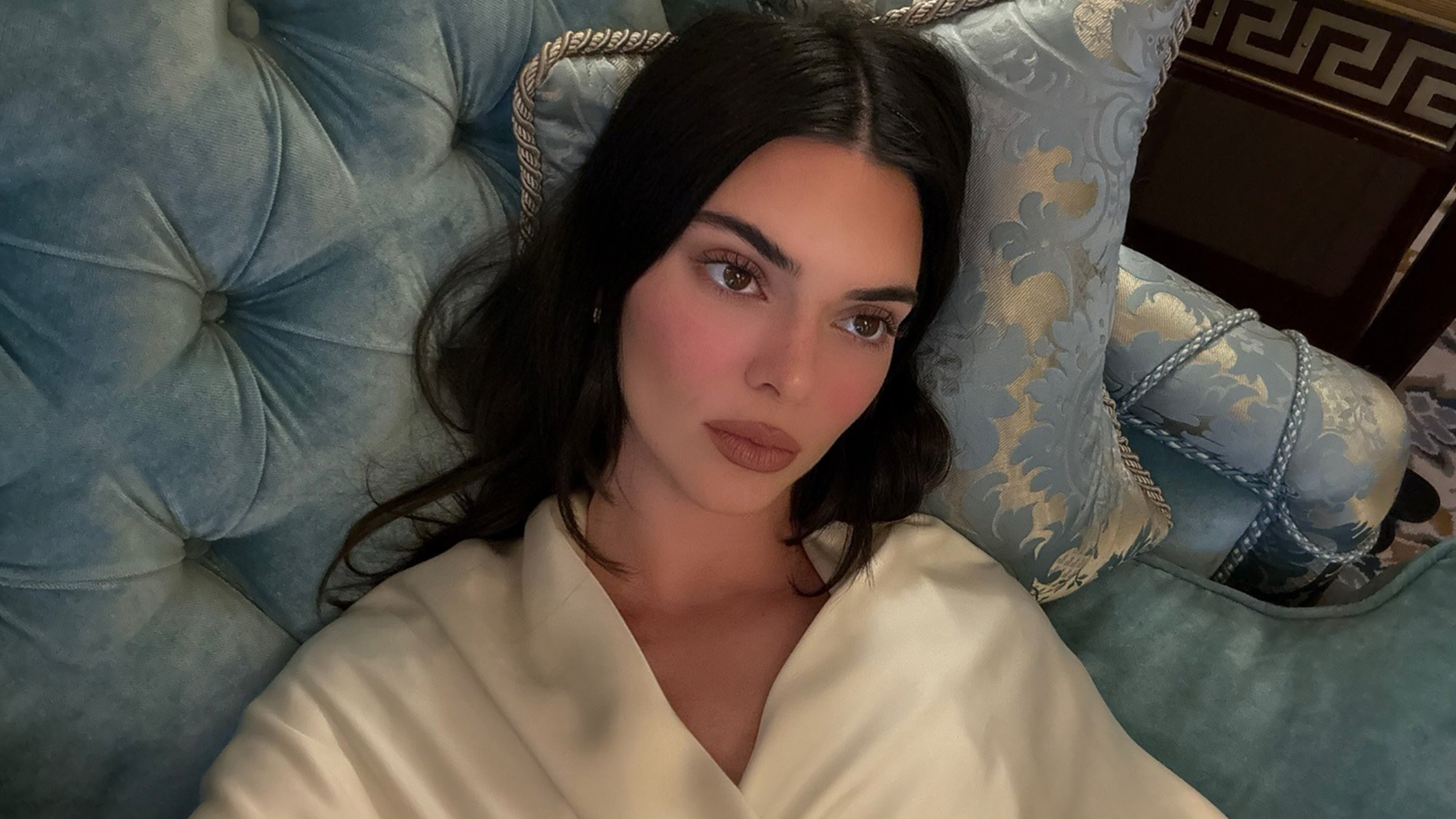 Kendall Jenner laying down wearing an ivory top.