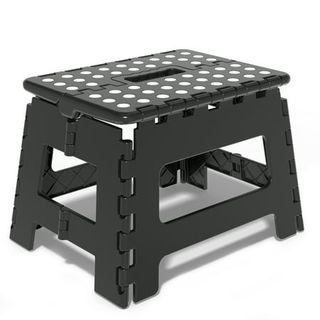 A black plastic folding step stool with white grip dots on the top. 