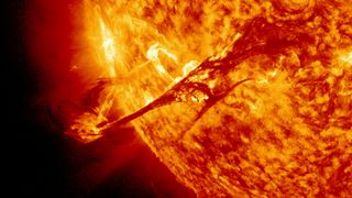 a raging fiery yellow and organge sun blazes from the right, filling two-thirds of the image. the star spits an arch of plasma high above its surface. so hot