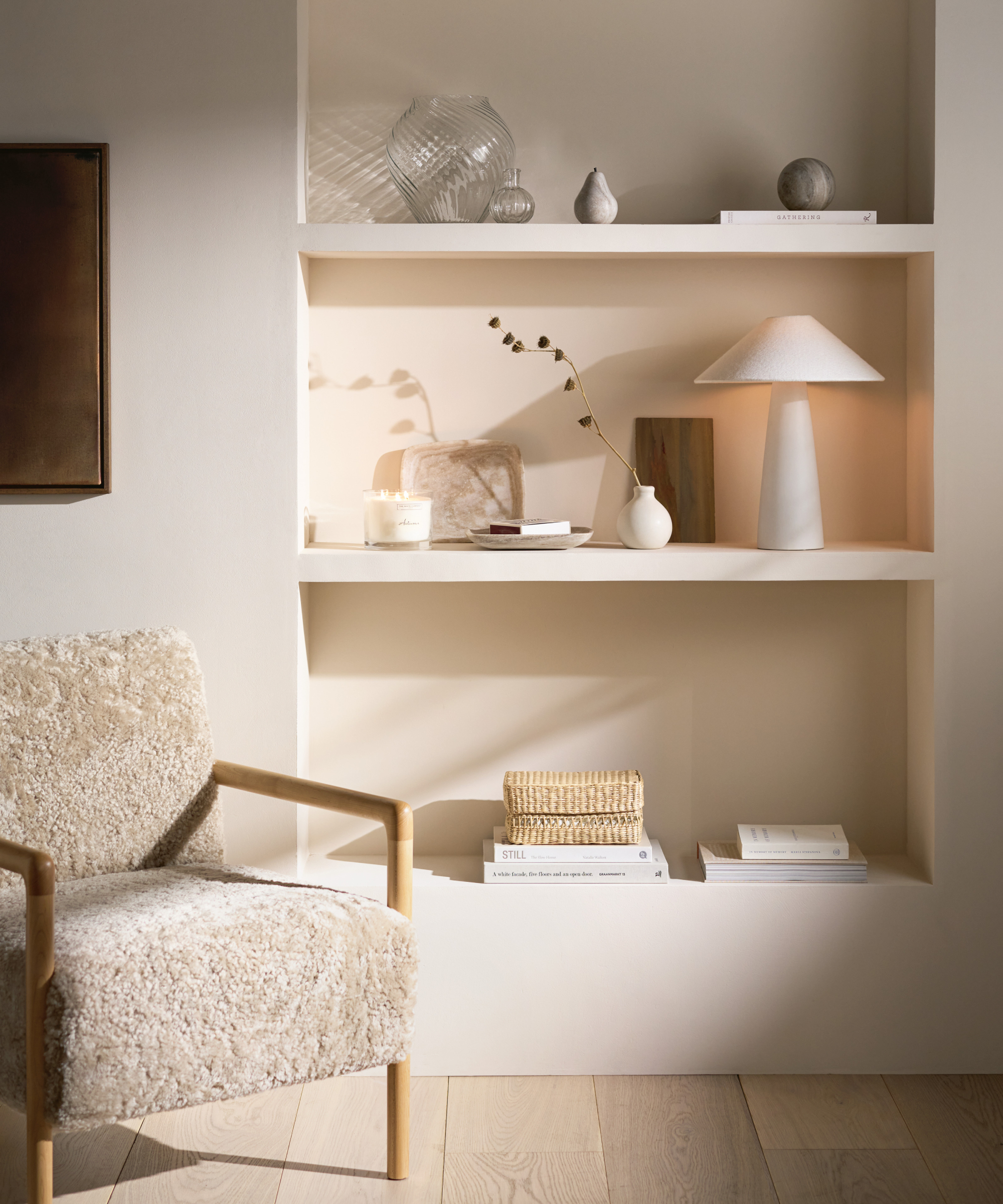 corner of off white painted living room with built in alcove shelving, light beige boucle armchair