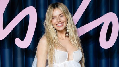 Image of Sienna Miller smiling with waving long blonde hair and wearing a white dress
