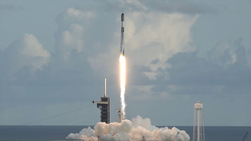 A white and black rocket lifts off into a partially cloudy sky above the East Coast of the United States, riding atop the bright white exhaust of its nine engines.