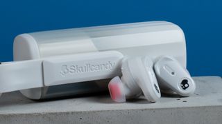 the skullcandy x bose method 360 anc earbuds in white, with a long charging case, a carabiner clip, and various silicone tip sizes