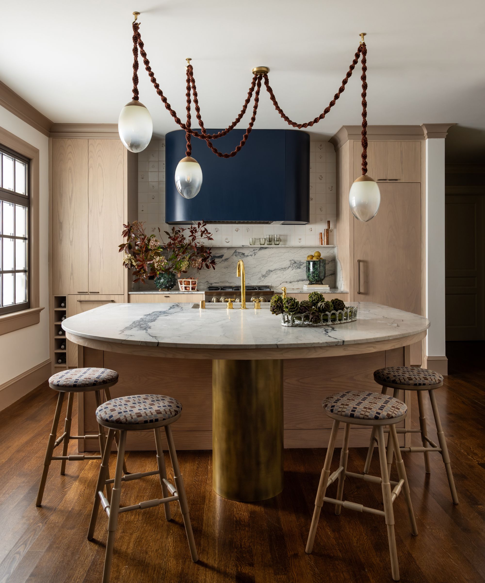 A wooden kitchen with marble countertops and a statement light fixture featuring dark purple hues and frosted glass
