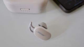one of the bose quietcomfort earbuds in front of its charging case