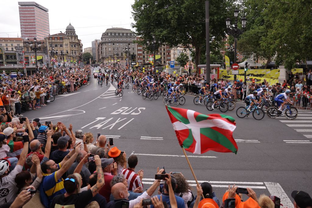 A spectator waves a Basque regional flag as the pack of riders cycles at the start of the 1st stage of the 110th edition of the Tour de France cycling race 182 km departing and finishing in Bilbao in northern Spain on July 1 2023 Photo by Thomas SAMSON AFP Photo by THOMAS SAMSONAFP via Getty Images
