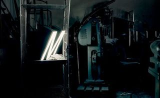 A large lit up "M" on a metal storage shelf in a dark store room.