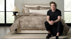 Jeremiah Brent sitting at the foot of a bed with a watercolor duvet color on the bed