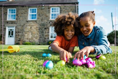 a close up of a brother and sister celebrating Easter by lying on the grass and unravelling Easter eggs