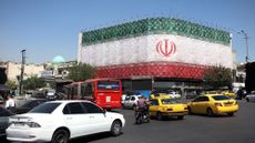 Traffic moves past the Iranian national flag displayed on a building at Enghelab square in Tehran as ceasefire deal announced