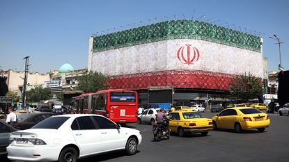 Traffic moves past the Iranian national flag displayed on a building at Enghelab square in Tehran as ceasefire deal announced