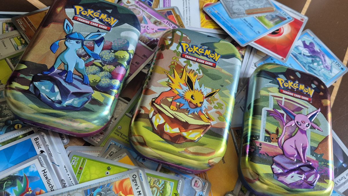 Prismatic Evolutions tins laid out in a row on a bed of cards