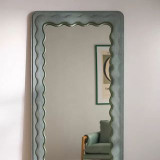 Adrie Upholstered Mirror against a white wall.