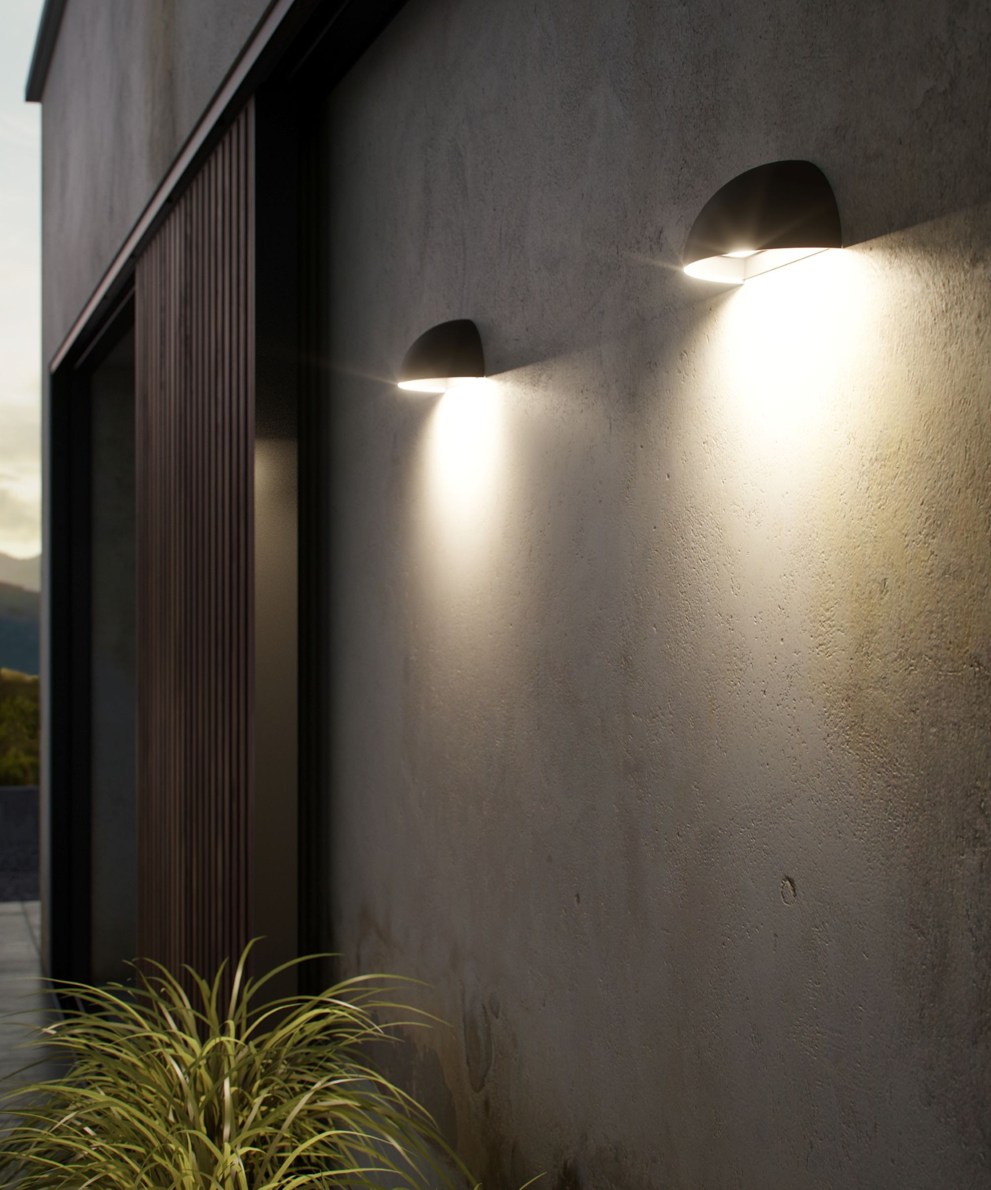 The side of a home with two lights on that are turned on and a plant underneath