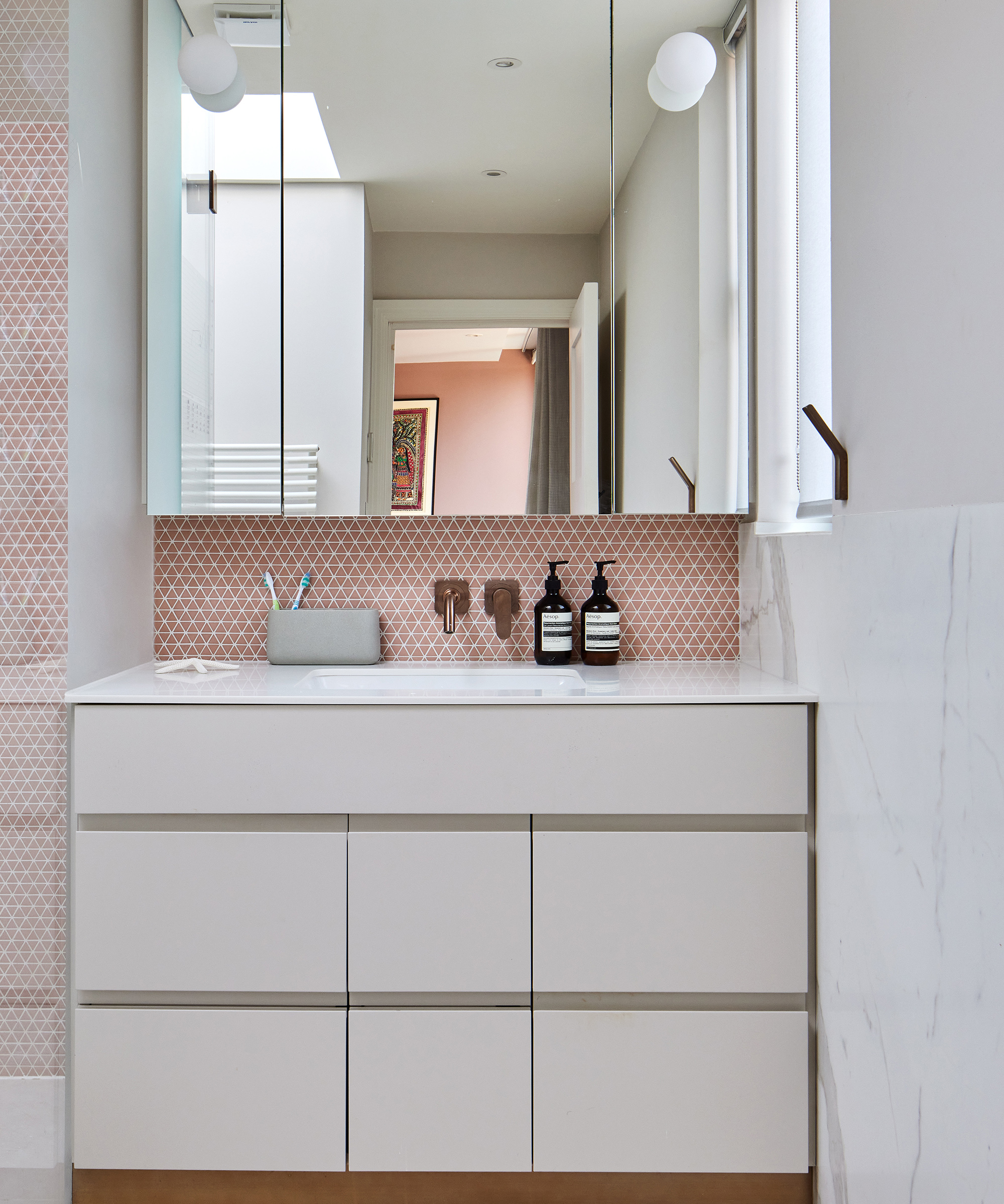 a small bathroom sink set into white cupboards and brass taps