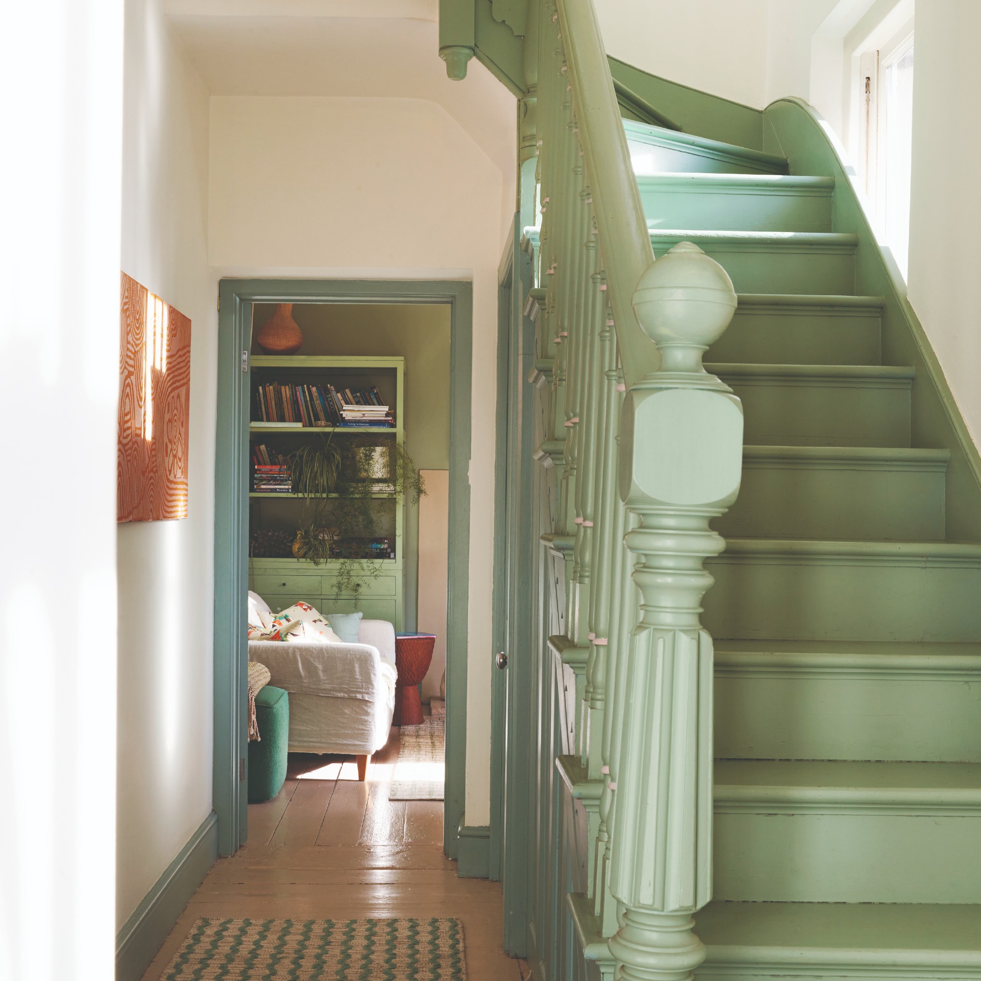 A hallway with a staircase painted sage green and tonal trims on skirting boards and door frame
