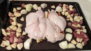 a chicken on a baking sheet with potatoes and onions