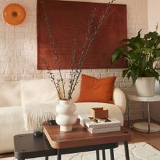 The off-white IKEA LILLESATER sofa in a white living room with a brick wall and a rust-coloured wall hanging above the sofa 