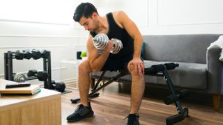 a photo of a man sitting on a home workout bench completing a bicep curl