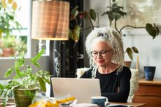 Grey haired woman at home smiling in front of laptop