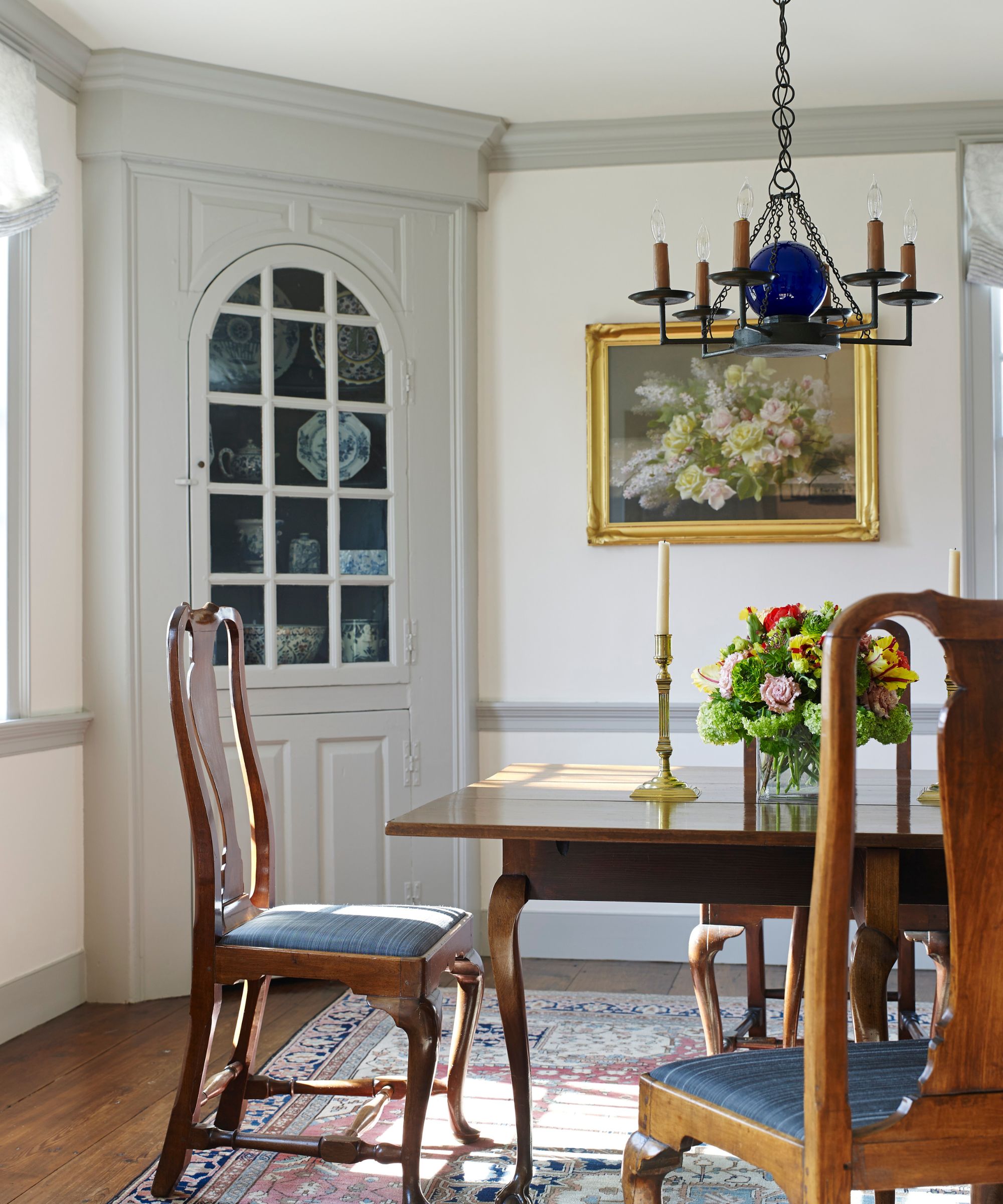 Grand dining room with dark mahogany chairs and table, painting still life, gold candle sticks, candelabra and cabinet with china