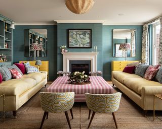 colorful living room with blue walls, patterned chairs, yellow chests of drawers and pink striped ottoman
