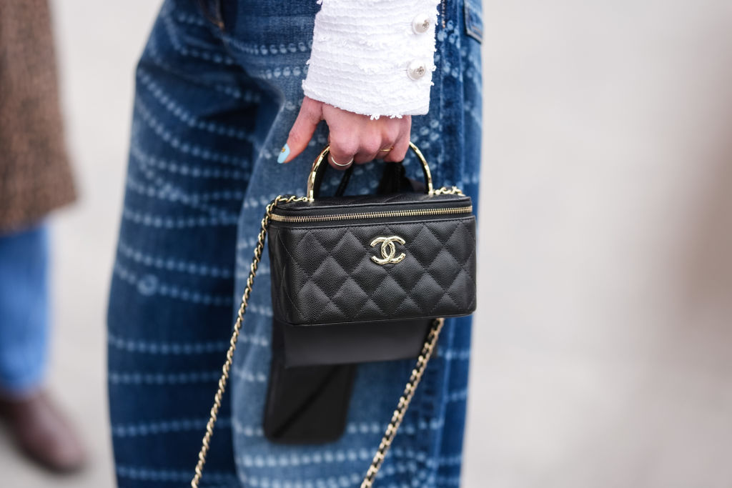A guest wears a shiny black quilted Chanel leather bag, outside Chanel, during the Paris Fashion week Women's
