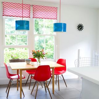 White dining room with red chairs, blue pendant lights and red and white patterned blinds