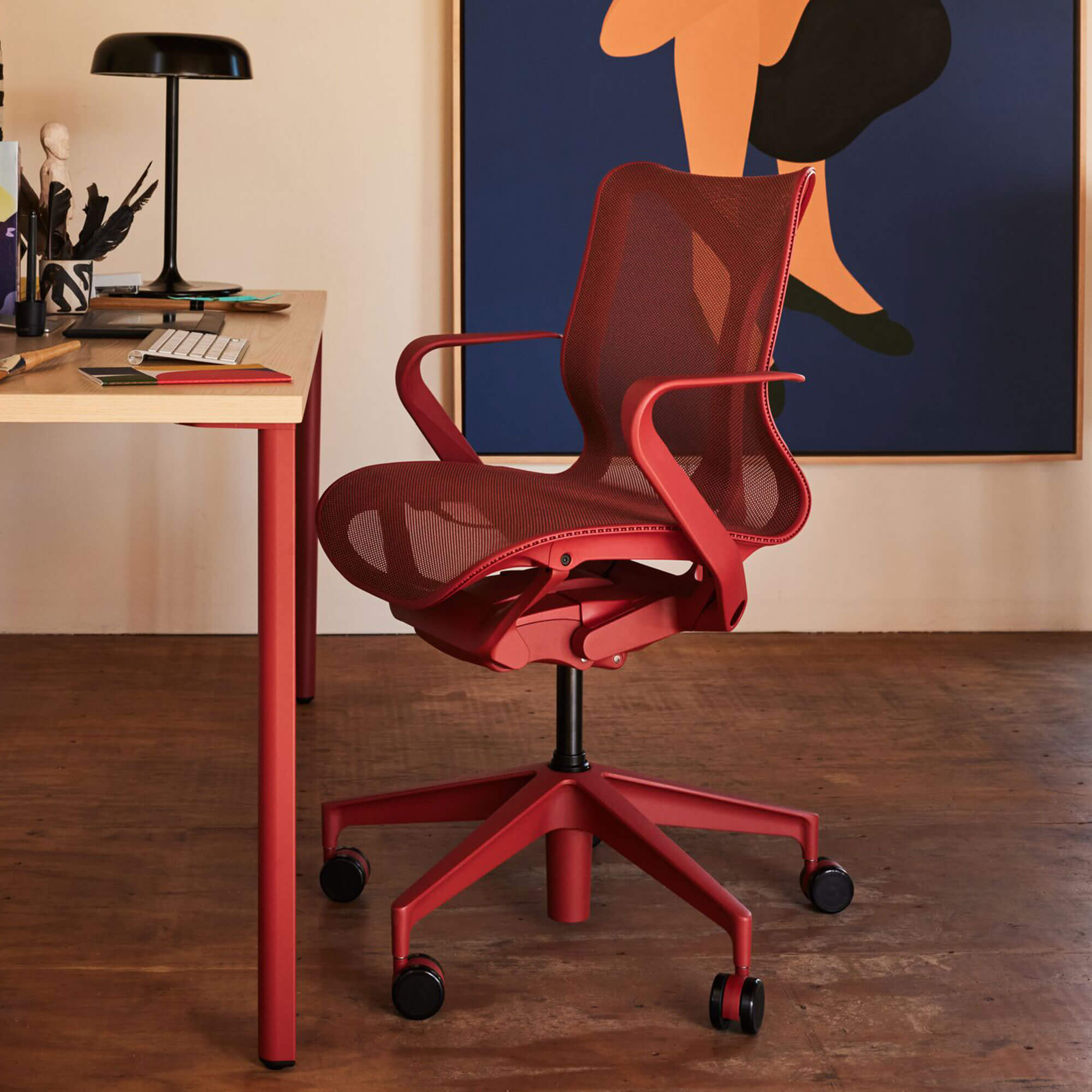 Red desk chair on wooden floor by wooden desk and large colourful graphic painting