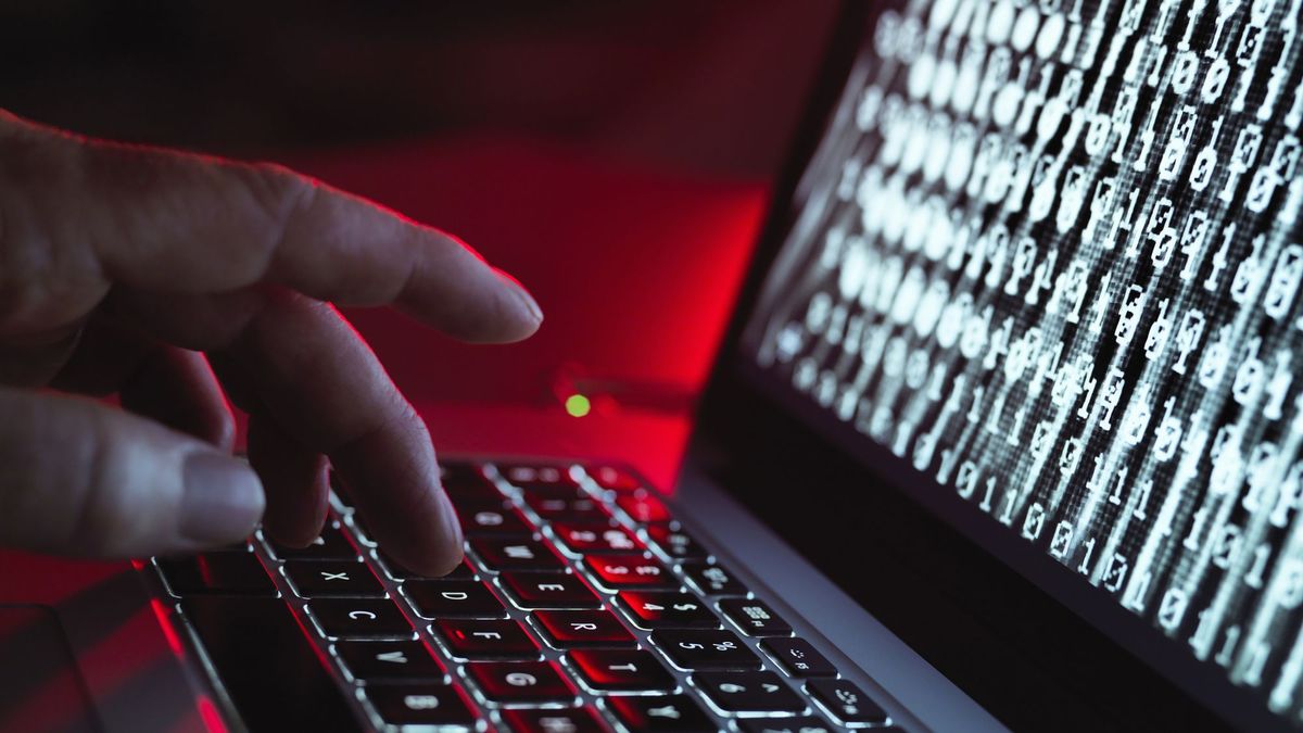 A hand typing on a laptop while binary code is displayed on the screen