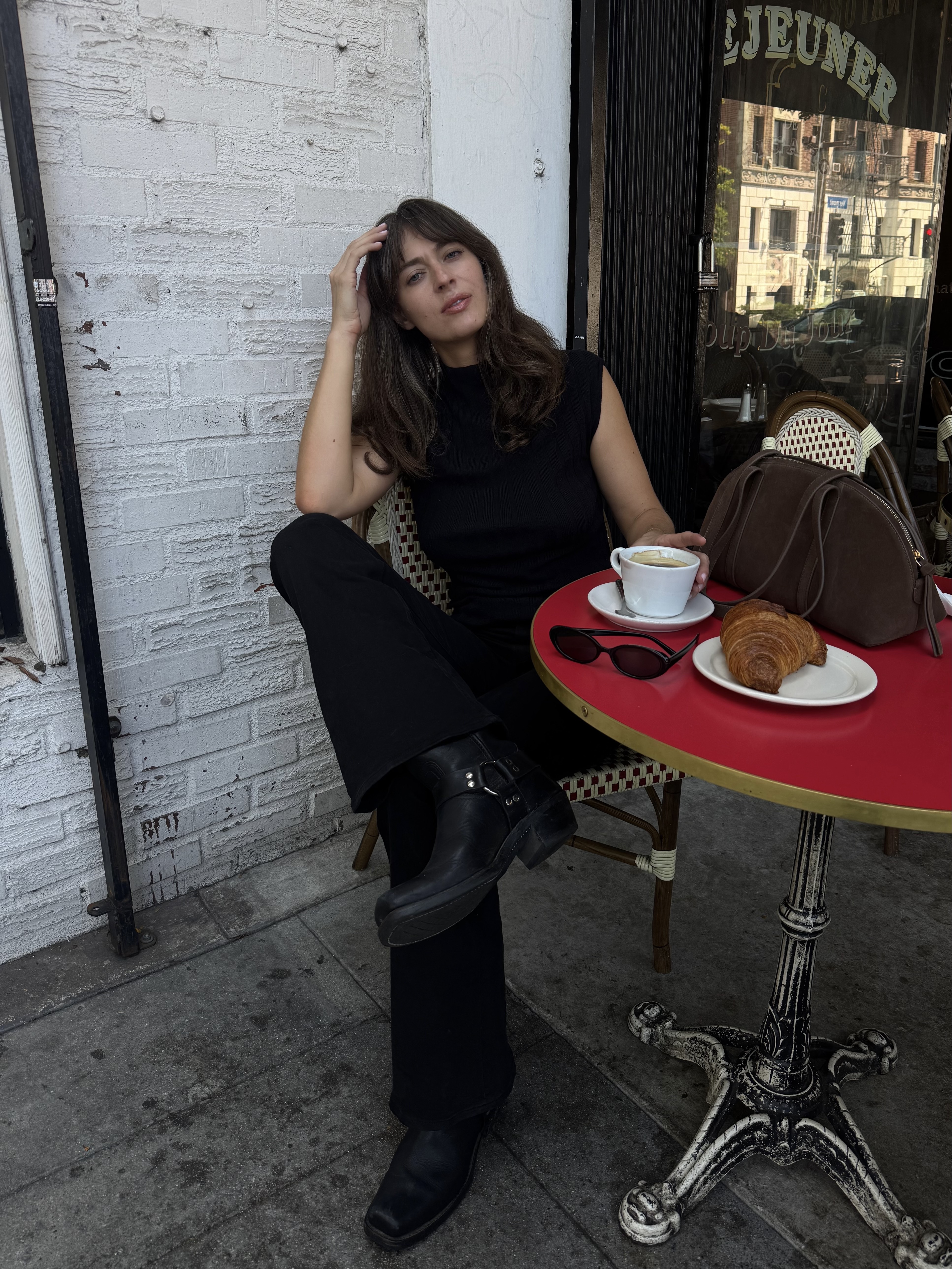 Kathryn Zahorak wearing black top, black pants, and black moto boots while sitting at a table