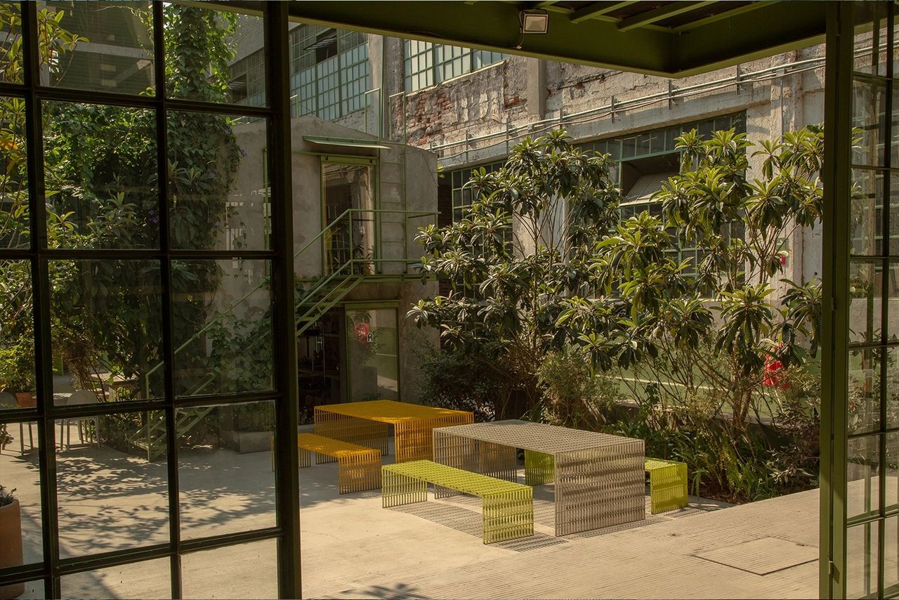 The inner courtyard of a former warehouse turned cultural center boasts tropical plants and nature-inspired minimalist outdoor furniture in lime, orange, and grey.