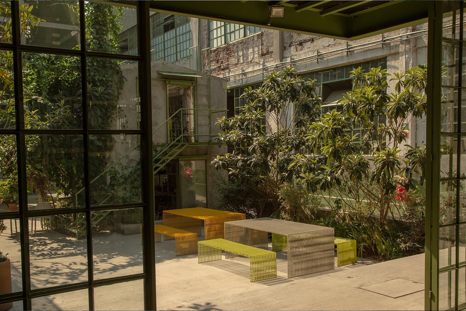 The inner courtyard of a former warehouse turned cultural center boasts tropical plants and nature-inspired minimalist outdoor furniture in lime, orange, and grey.