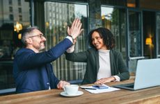 A retirement coach high fives her client as they sit in front of a laptop at a cafe.