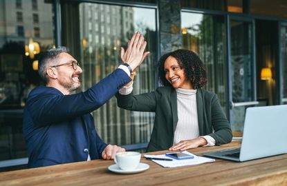 A retirement coach high fives her client as they sit in front of a laptop at a cafe.