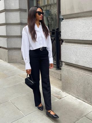 a photo of a woman wearing a white button-down and black trousers and ballet flats