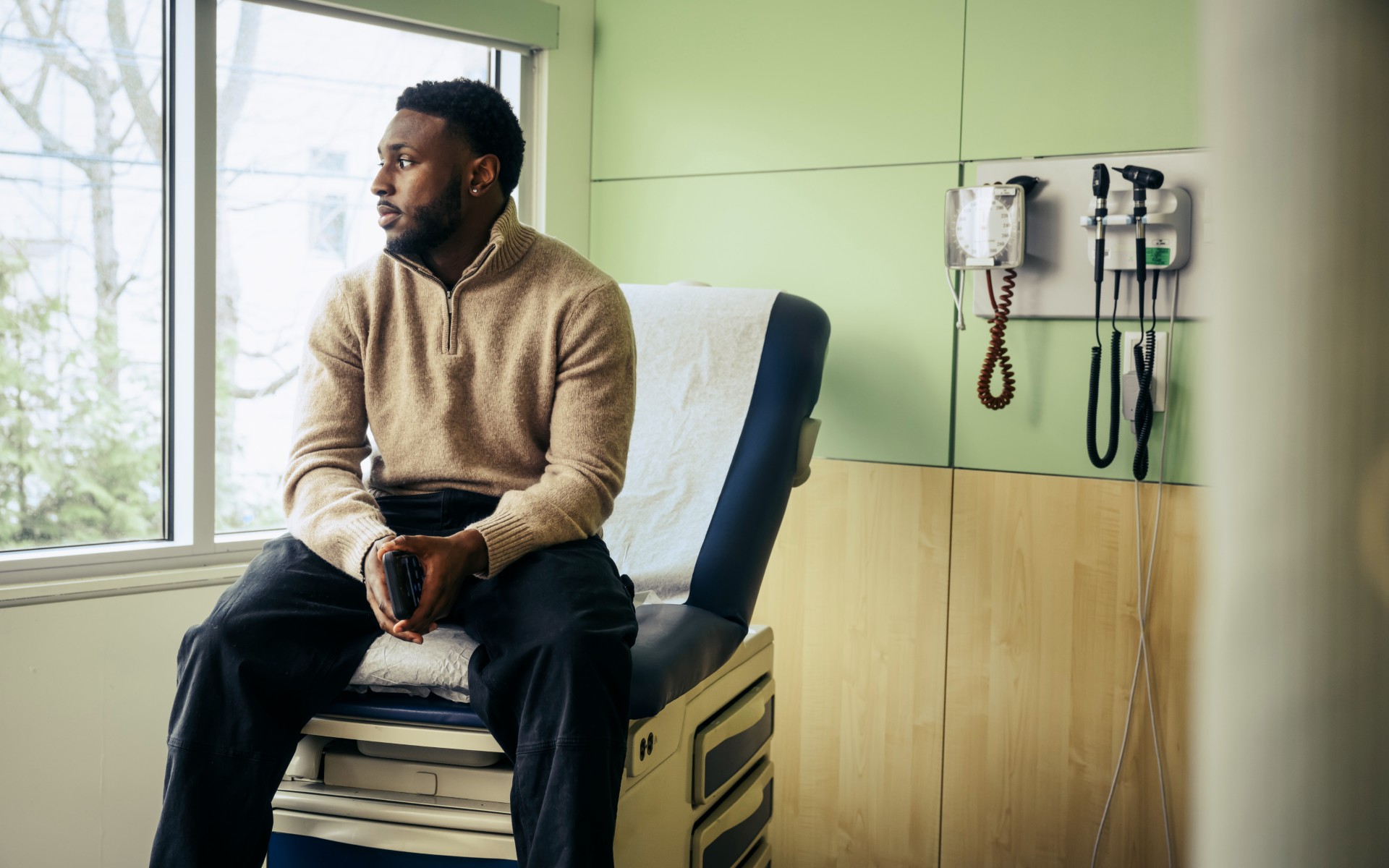  Young Black man sitting on exam table in doctor's office 