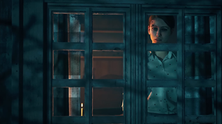 A still from Silent Hill: Ascension, where a woman looks out through a window at a dark and brooding forest.