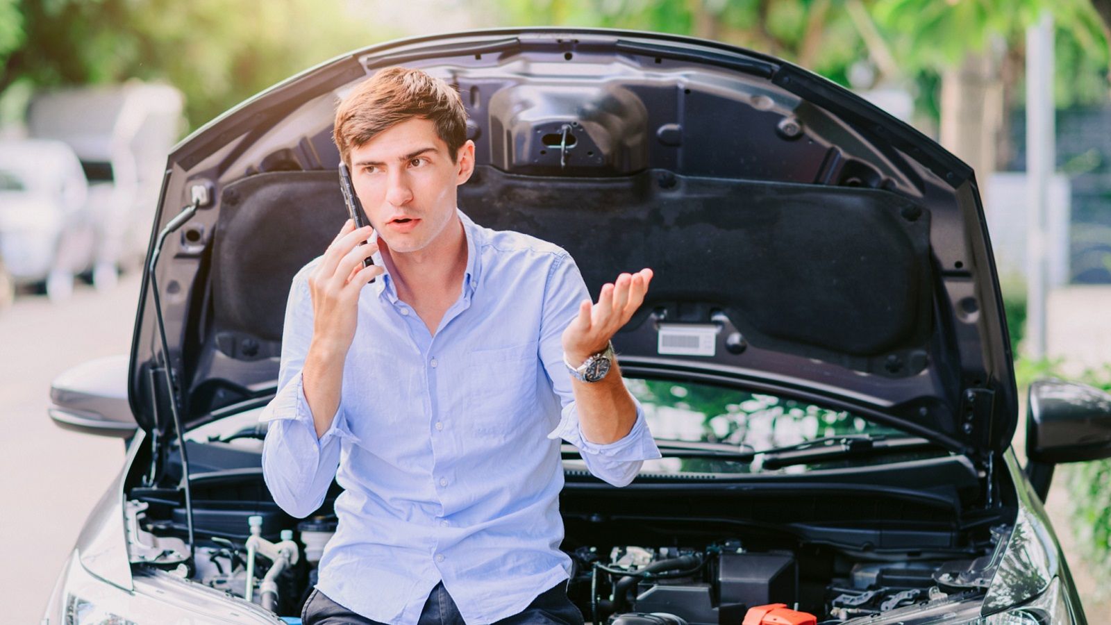 A man calls his car insurance provider near his broken-down car.