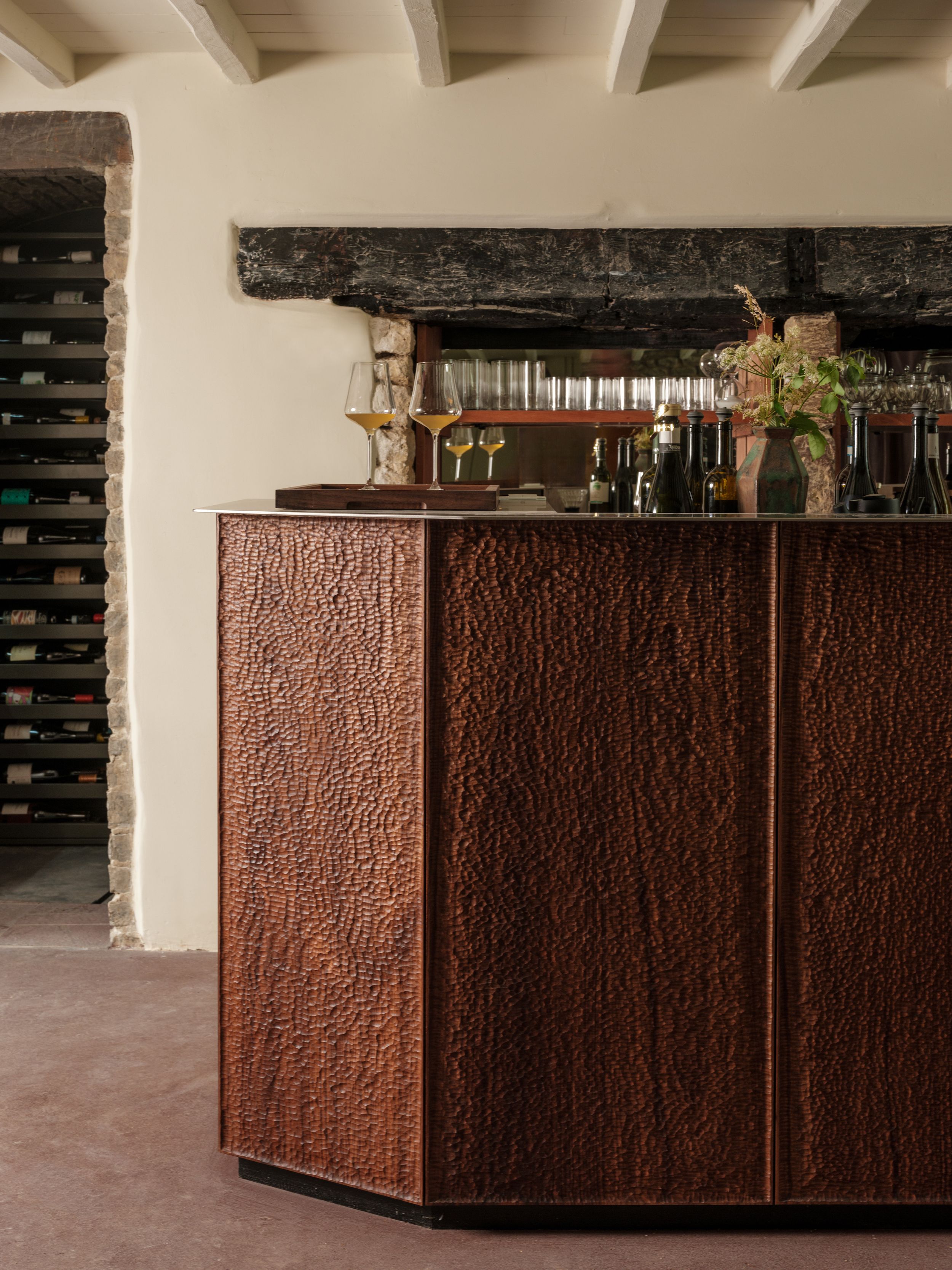 A series of shots depicting the interiors of a modernly renovated, old farmhouse in the countryside, mixing a rustic frame with plush textiles, textural surfaces, glass, wood, and chrome accents, and colorfully plated dishes.