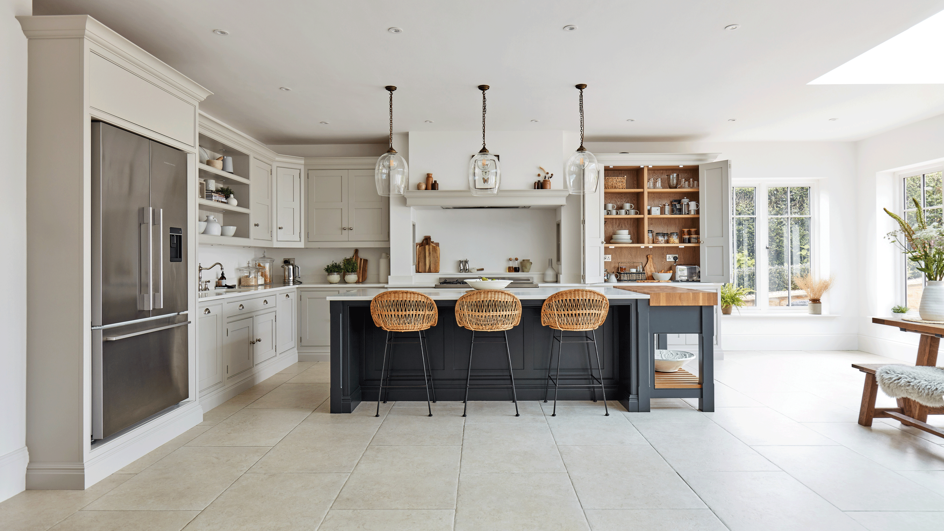 White kitchen with a large kitchen island painted navy with three rattan kitchen island stools