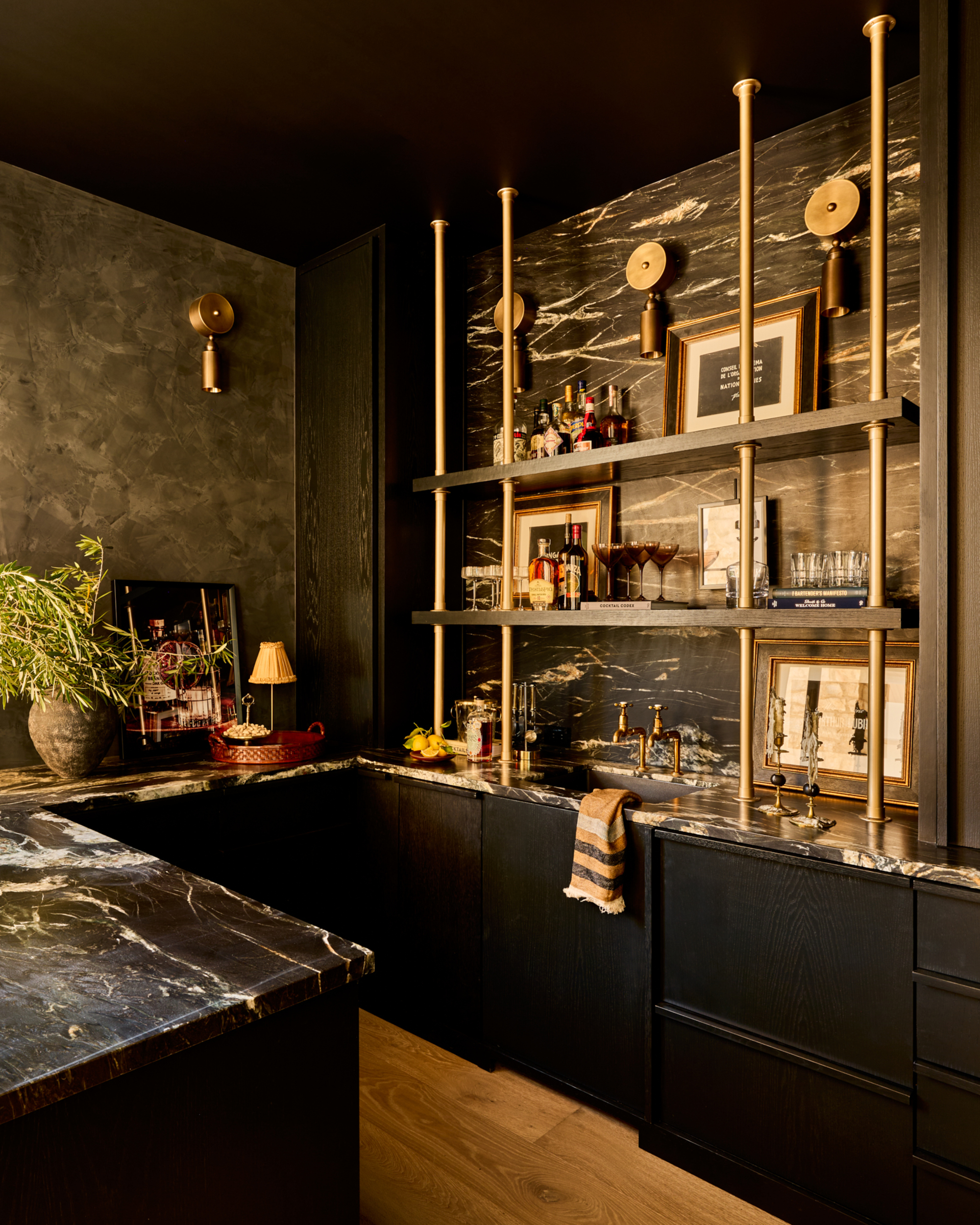 A kitchen with black cabinetry, black and white marble, and brass accents