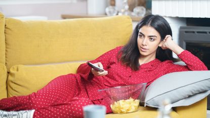 Woman Watching the most relaxing shows on TV While Lying Down On Sofa With Potato Chips at home