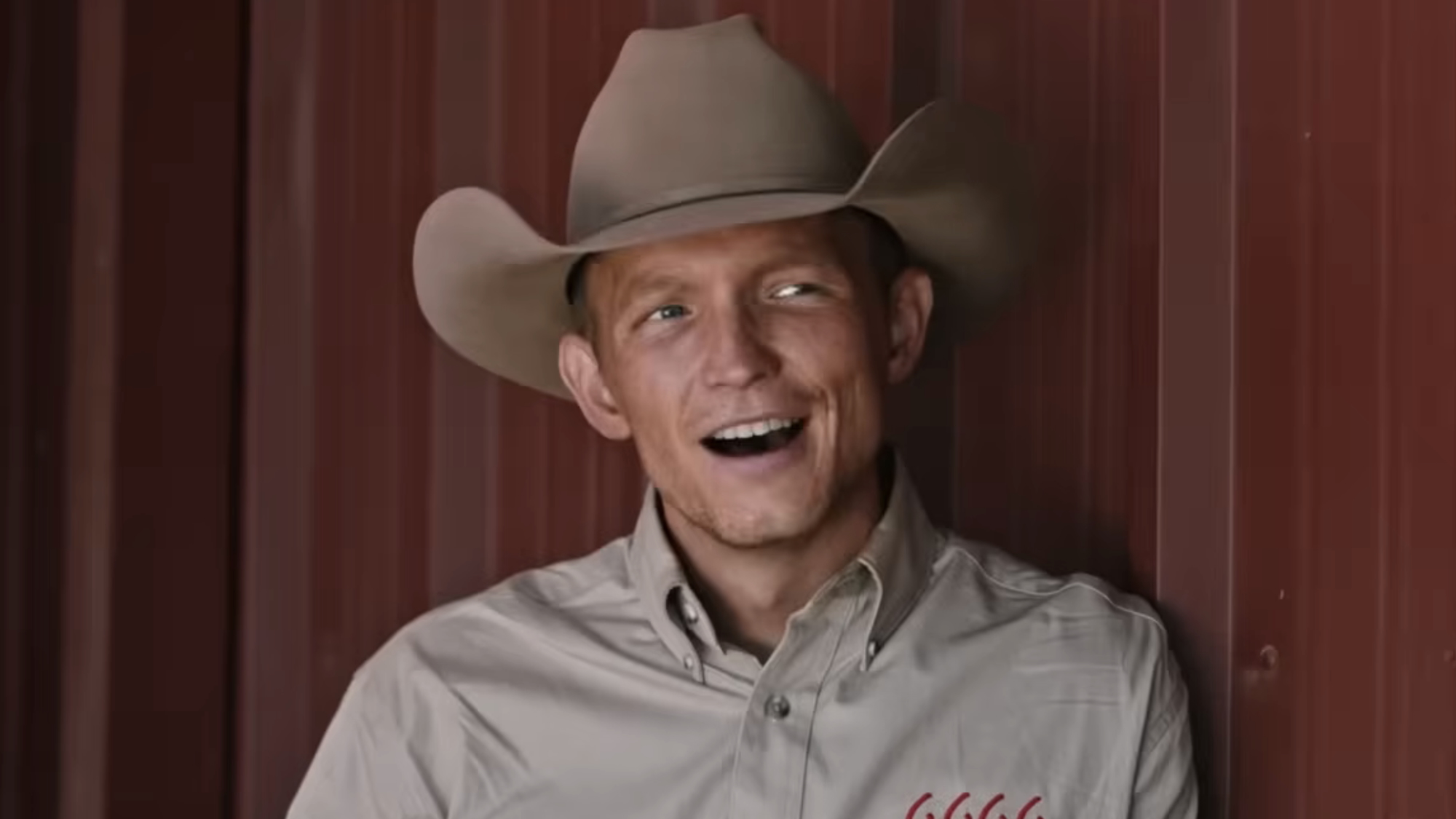 Jimmy in 6666 shirt leaning against wall smiling at Emily in Yellowstone