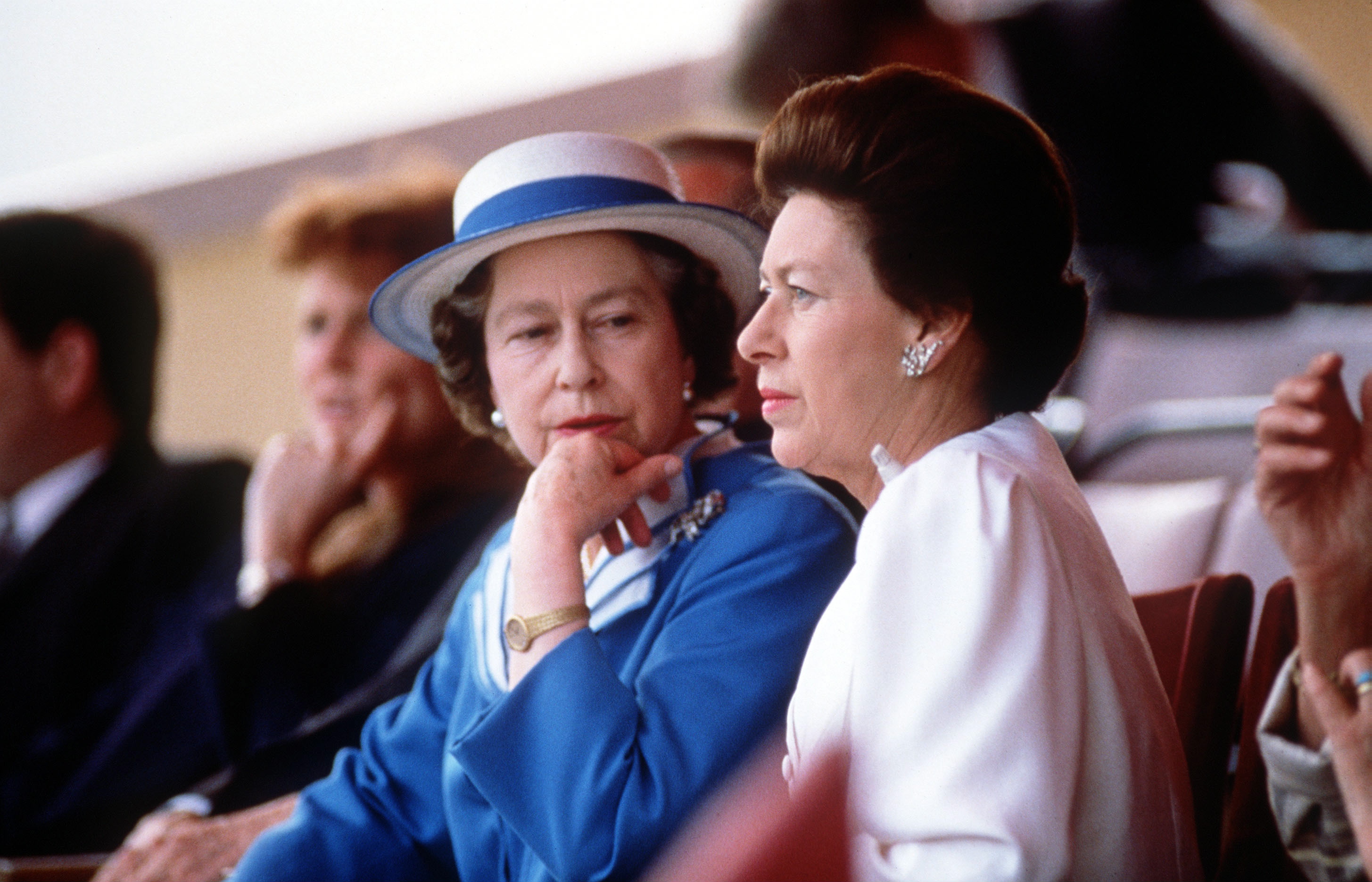 Queen Elizabeth wearing a purple coat looking at Princess Margaret, wearing a pink dress